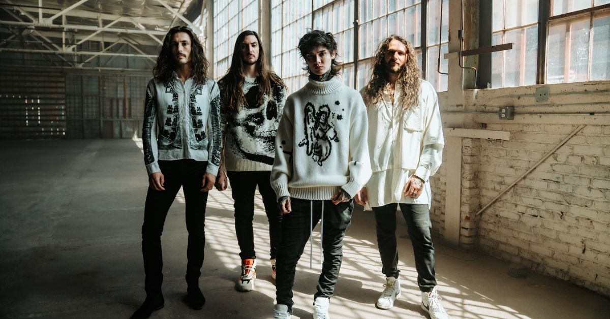 Polyphia standing in a warehouse wearing white - PHOTO CREDIT: ALANA ANN LOPEZ