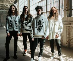 Polyphia standing in a warehouse wearing white - PHOTO CREDIT: ALANA ANN LOPEZ